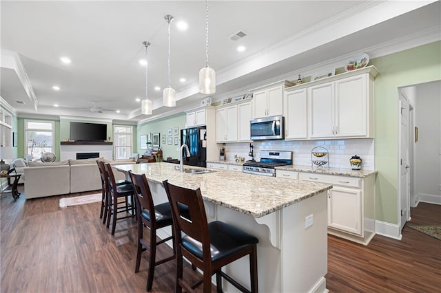 kitchen with ceiling fan, a kitchen breakfast bar, an island with sink, stainless steel appliances, and white cabinets