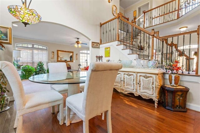 dining space with wood-type flooring, a towering ceiling, ceiling fan, and crown molding