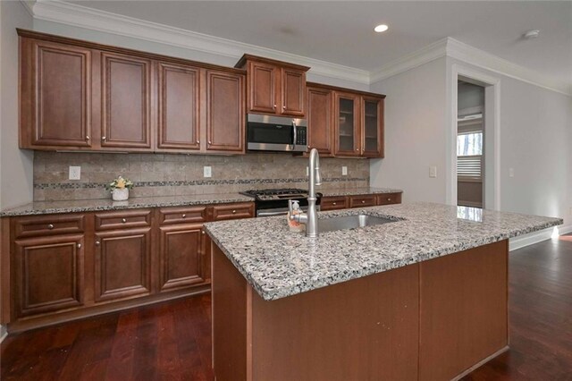 kitchen with sink, dark wood-type flooring, appliances with stainless steel finishes, light stone counters, and an island with sink