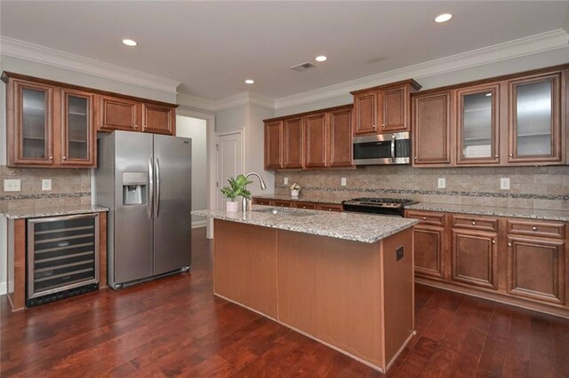 kitchen with sink, stainless steel appliances, beverage cooler, light stone countertops, and a kitchen island with sink