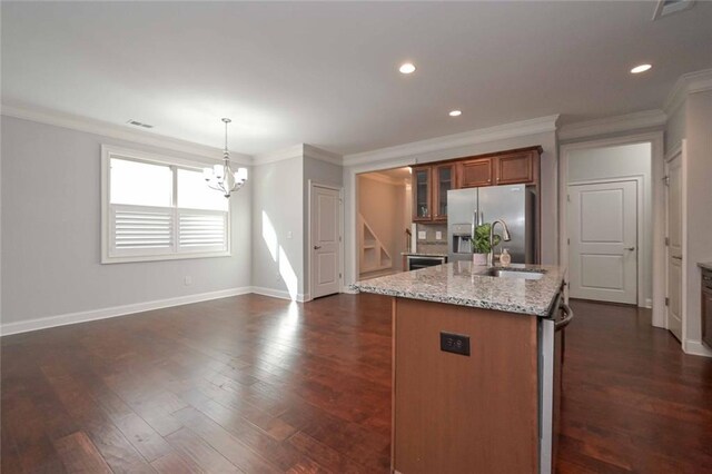 kitchen featuring pendant lighting, an island with sink, light stone counters, stainless steel fridge with ice dispenser, and dark wood-type flooring