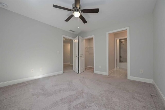 unfurnished bedroom featuring a spacious closet, light colored carpet, ceiling fan, ensuite bath, and a closet