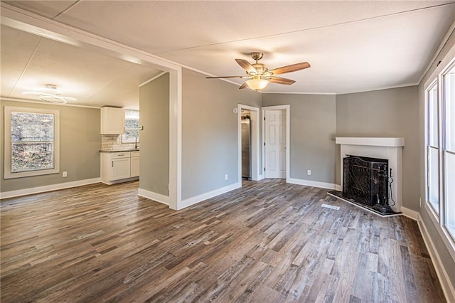 unfurnished living room featuring dark wood-style floors, a fireplace with raised hearth, a healthy amount of sunlight, and baseboards