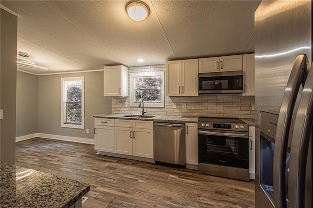 kitchen featuring dark wood-style floors, a sink, stainless steel appliances, white cabinetry, and tasteful backsplash