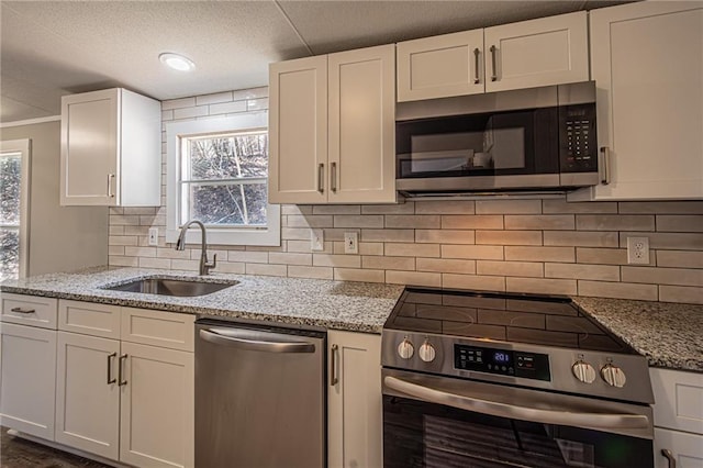 kitchen featuring backsplash, light stone counters, appliances with stainless steel finishes, white cabinets, and a sink