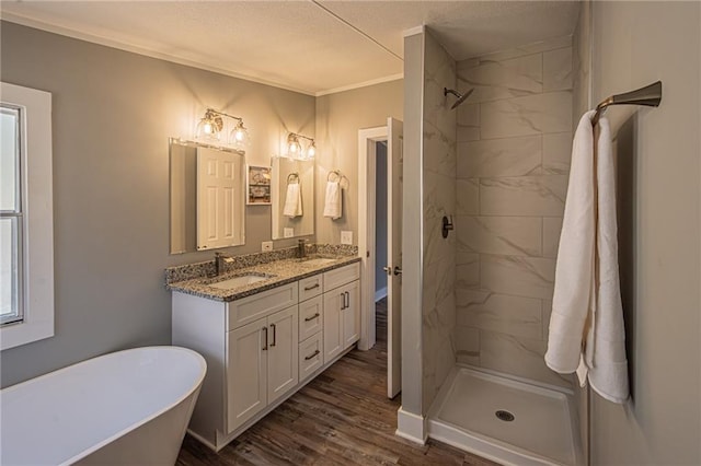 bathroom featuring wood finished floors, double vanity, a sink, a freestanding bath, and a shower stall