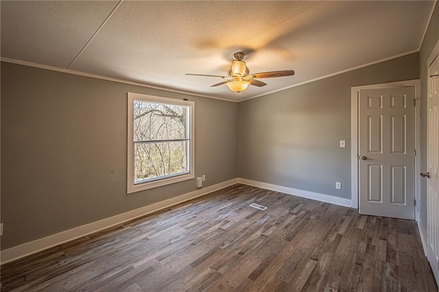 empty room featuring dark wood-type flooring, a ceiling fan, a textured ceiling, crown molding, and baseboards