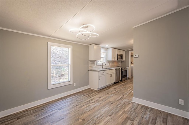 kitchen with a sink, tasteful backsplash, stainless steel appliances, white cabinets, and crown molding