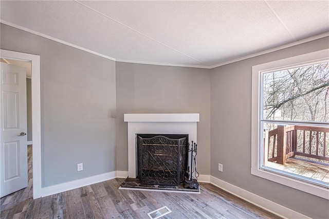 unfurnished living room featuring wood finished floors, visible vents, baseboards, a fireplace with raised hearth, and ornamental molding