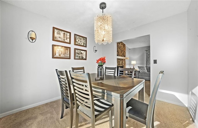 dining space with light carpet, a fireplace, baseboards, and an inviting chandelier