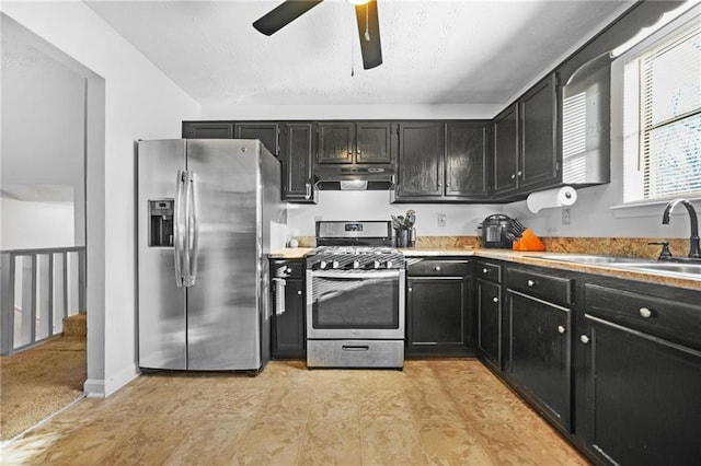 kitchen with appliances with stainless steel finishes, dark cabinets, light countertops, under cabinet range hood, and a sink