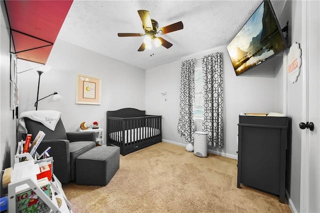 bedroom featuring a crib, a textured ceiling, baseboards, and carpet flooring