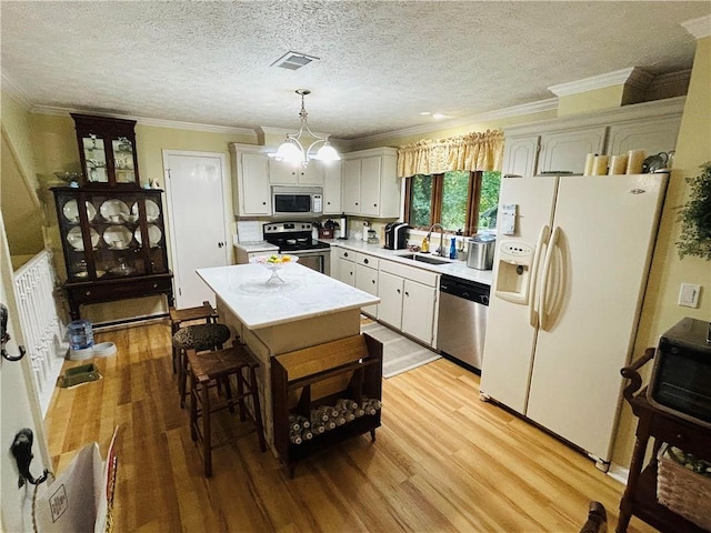 kitchen with white cabinetry, decorative light fixtures, a kitchen island, sink, and appliances with stainless steel finishes