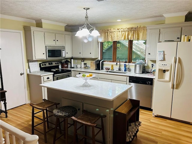 kitchen featuring a textured ceiling, decorative light fixtures, appliances with stainless steel finishes, sink, and light wood-type flooring