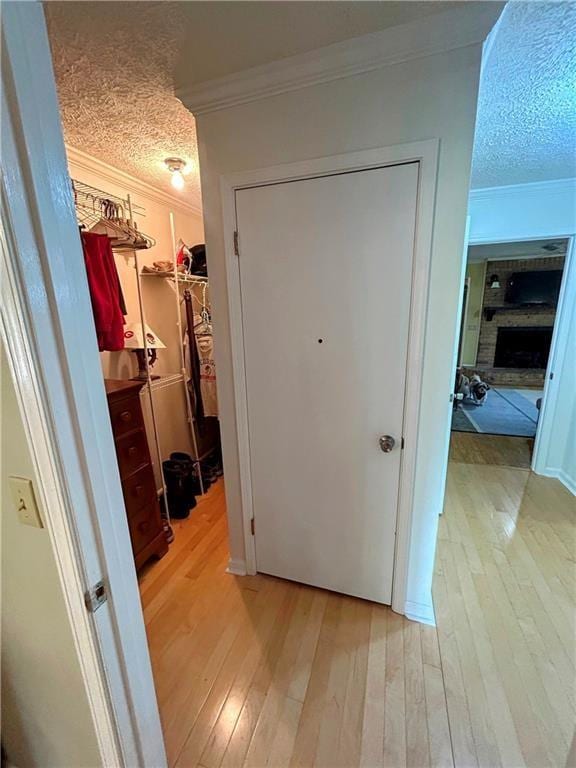 corridor with a textured ceiling, crown molding, and light wood-type flooring