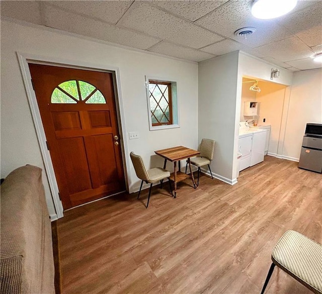 foyer with light hardwood / wood-style floors, a drop ceiling, and washer and dryer