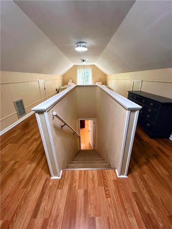 stairway featuring vaulted ceiling, a textured ceiling, and hardwood / wood-style flooring