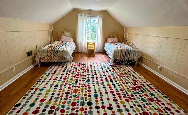 unfurnished bedroom featuring lofted ceiling, hardwood / wood-style floors, and wooden walls