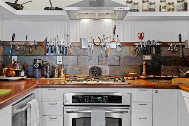 kitchen featuring stainless steel appliances, wood counters, white cabinets, wall chimney range hood, and decorative backsplash