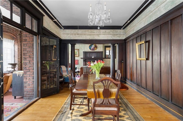 dining area featuring ornamental molding, light wood finished floors, ornate columns, and an inviting chandelier