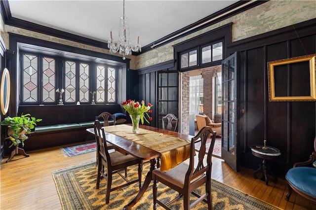 dining area featuring wallpapered walls, hardwood / wood-style floors, crown molding, a chandelier, and a decorative wall