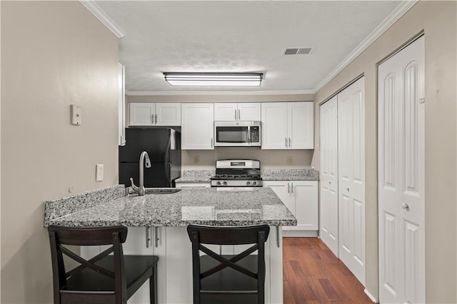 kitchen with appliances with stainless steel finishes, white cabinetry, a breakfast bar area, kitchen peninsula, and light stone countertops