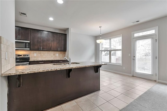 kitchen with dark brown cabinetry, sink, a kitchen breakfast bar, pendant lighting, and appliances with stainless steel finishes