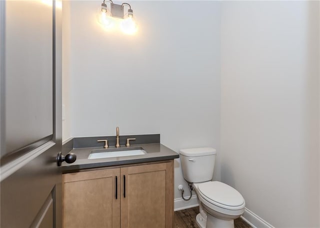 half bath featuring vanity, baseboards, wood finished floors, and toilet
