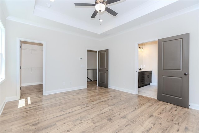 unfurnished bedroom featuring crown molding, a walk in closet, a tray ceiling, and light wood-style flooring