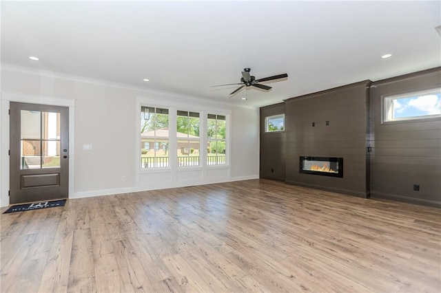 unfurnished living room featuring ornamental molding, wood finished floors, baseboards, a large fireplace, and a ceiling fan