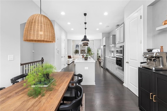 kitchen with appliances with stainless steel finishes, a center island, decorative light fixtures, and dark hardwood / wood-style floors