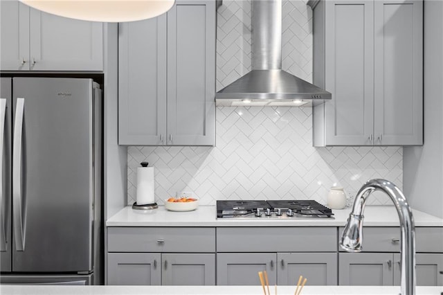 kitchen featuring appliances with stainless steel finishes, decorative backsplash, gray cabinets, and wall chimney exhaust hood