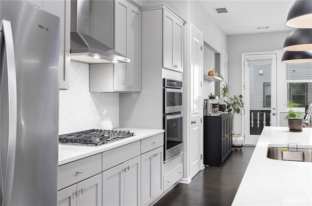 kitchen with appliances with stainless steel finishes, gray cabinetry, pendant lighting, wall chimney range hood, and backsplash