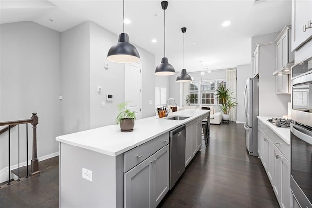 kitchen with vaulted ceiling, appliances with stainless steel finishes, an island with sink, sink, and decorative light fixtures