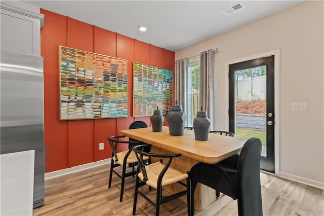 dining area with light wood-style floors, a decorative wall, and baseboards