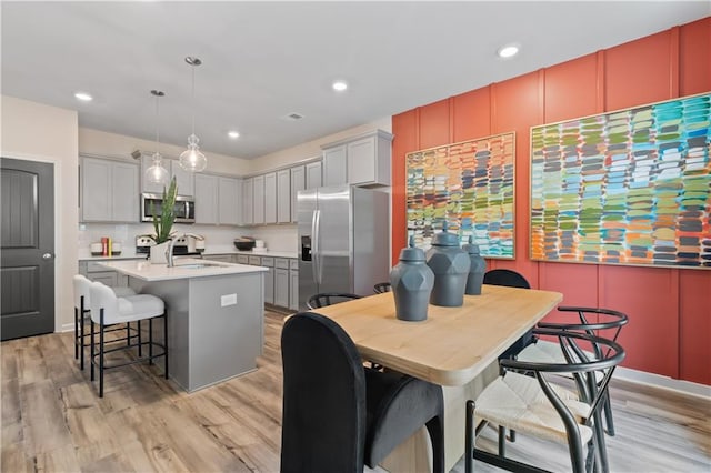 kitchen featuring appliances with stainless steel finishes, light wood-type flooring, a sink, a breakfast bar, and a kitchen island with sink