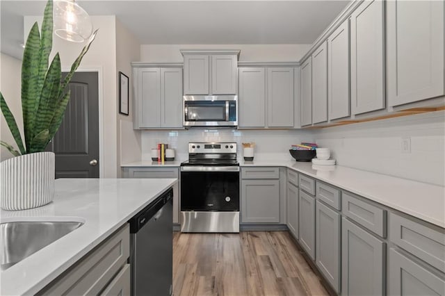 kitchen featuring stainless steel appliances, gray cabinetry, backsplash, light wood finished floors, and light countertops