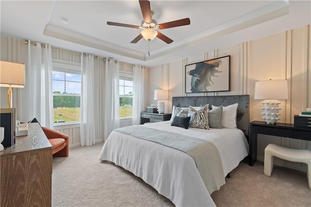 bedroom with a raised ceiling, light carpet, and a ceiling fan