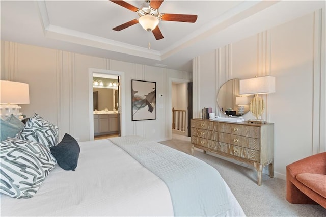 bedroom featuring a raised ceiling, light carpet, ensuite bath, ceiling fan, and crown molding