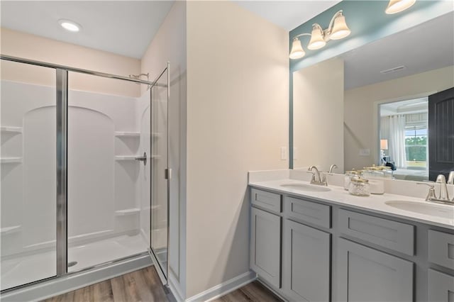 bathroom featuring a shower stall, wood finished floors, double vanity, ensuite bath, and baseboards