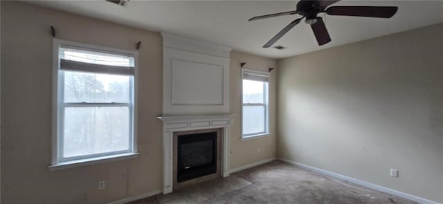 unfurnished living room with ceiling fan, a fireplace, light colored carpet, and baseboards