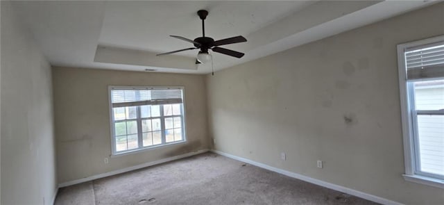 unfurnished room featuring baseboards, a raised ceiling, a wealth of natural light, and light colored carpet