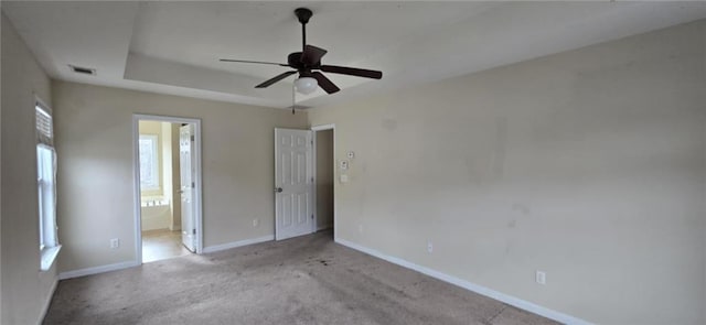 unfurnished bedroom featuring baseboards, visible vents, a raised ceiling, light colored carpet, and ensuite bathroom