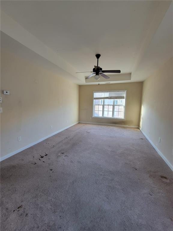 unfurnished room featuring light carpet, a tray ceiling, a ceiling fan, and baseboards