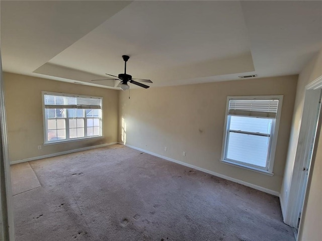 spare room with a tray ceiling, light carpet, visible vents, and baseboards