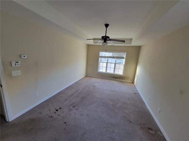 spare room featuring a raised ceiling, light carpet, ceiling fan, and baseboards