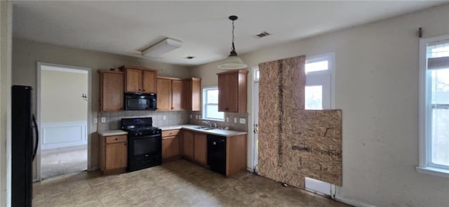 kitchen with pendant lighting, brown cabinets, light countertops, visible vents, and black appliances