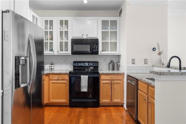 kitchen with white cabinetry, light stone counters, and black appliances