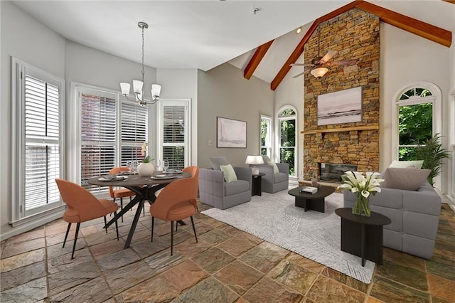 dining area featuring high vaulted ceiling, ceiling fan with notable chandelier, beamed ceiling, and a stone fireplace