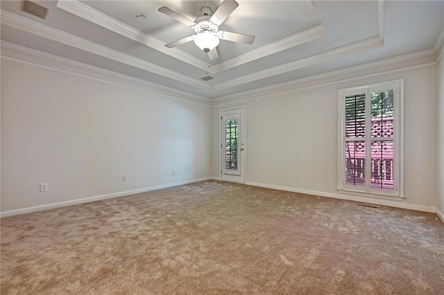 carpeted spare room featuring ceiling fan, a wealth of natural light, a raised ceiling, and ornamental molding